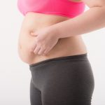 ポッコリと出たお腹をつまんでいる女性